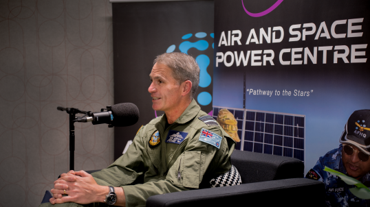 Chief of Air Force Rob Chipman sitting in navy blue coloured arm chairs with air and space power centre pull up banners behind him. In front of him is a microphone on a stand 