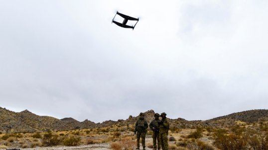 Australian soldiers standing on rocky, mountainous terrain operate an Unmanned Aerial Vehicle, or drone, as part of the 'Hyper-Teaming' experiment at Project Convergence Capstone 5, at Fort Irwin, California.
