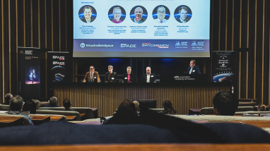 4 panel members on stage with 1 moderator. large screen behind speakers with powerpoint presentation