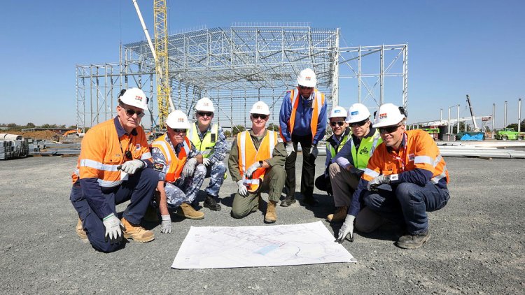 Group of workers in hi-vis, posing on one knee around a map in front of a building site
